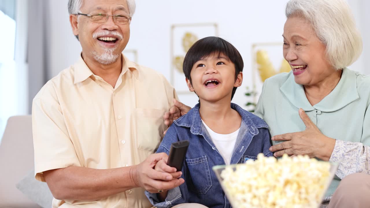 自宅での居心地の良い映画鑑賞ナイトで、ポップコーンを分け合いながら笑うアジアの家族3世代