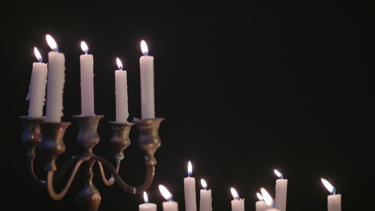 un grupo de velas blancas, algunas en un candelabro iluminadas y luego apagadas por el viento en cámara lenta