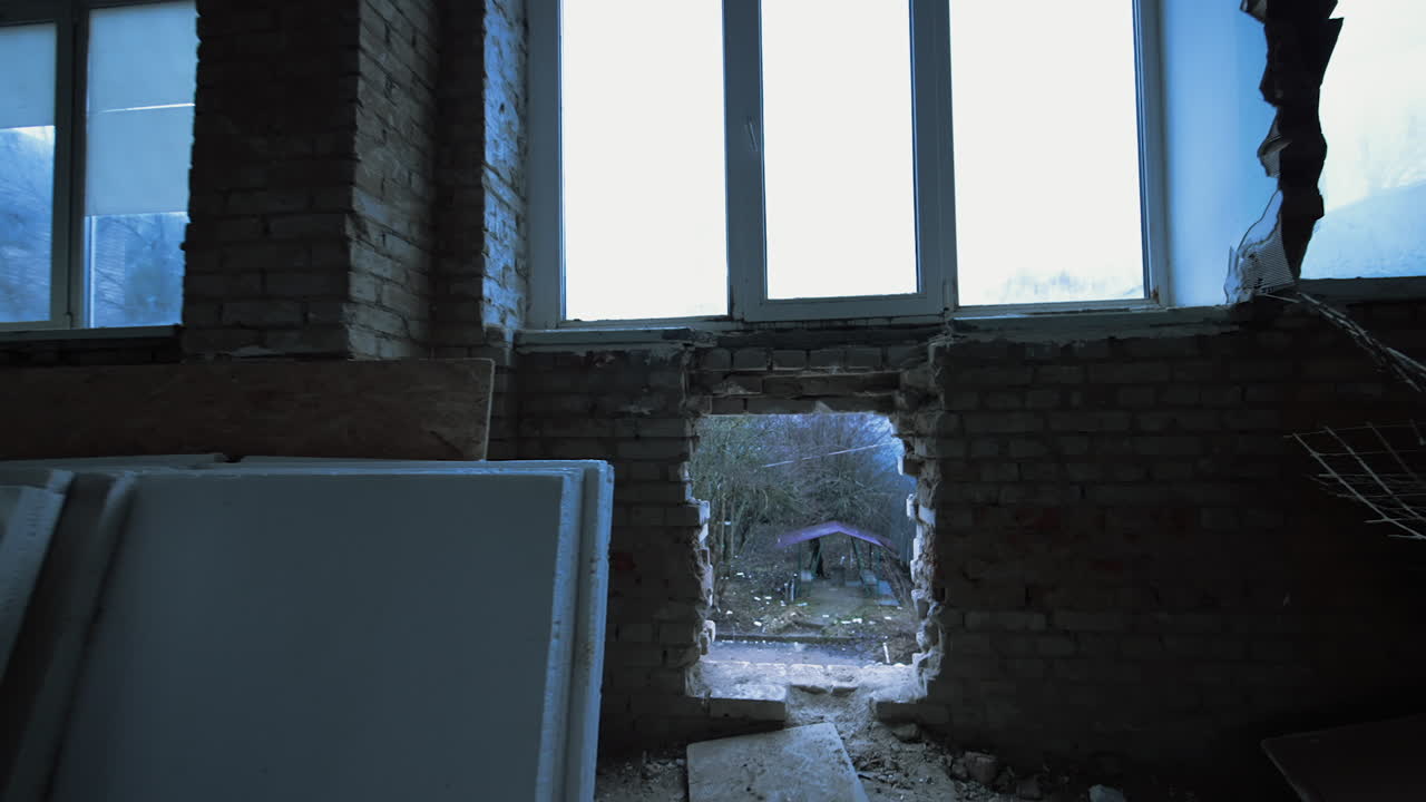 Snowy day outdoors. Metal hangar in the industrial zone and a pile of pipes on the ground. Look through the hole in the brick wall of the ruined building.