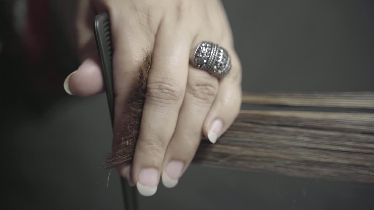 Primo piano di parrucchiera che tiene i capelli tra le mani e li taglia con le forbici.