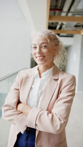 vertical video: smiling businesswoman in blazer standing confidently with arms crossed indoors