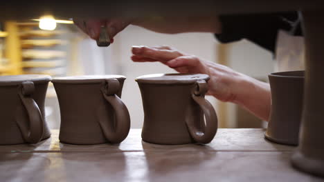 close up of male potter putting studio stamp onto base of clay mugs