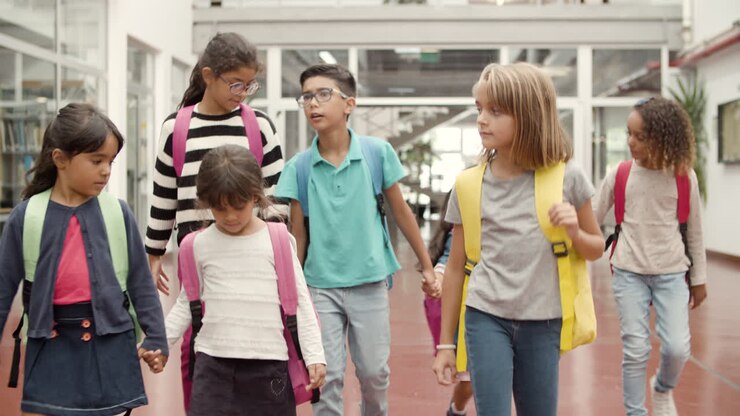 Feliz grupo multiétnico de escolares con mochilas caminando por el pasillo de la escuela y yendo a clase