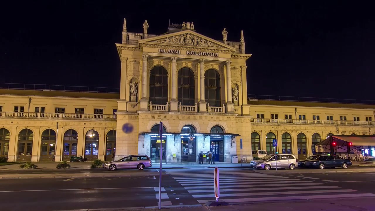 Gente en la Plaza Tomislav frente a la Estación Central de Trenes, timelapse hyperlapse nocturno, principal centro de la red de Ferrocarriles Croatas. Tráfico en la carretera. ZAGREB, CROACIA.