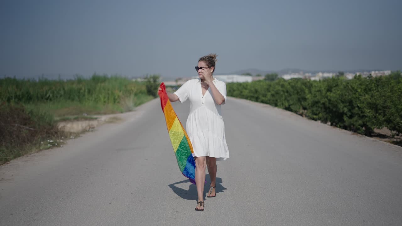 Woman walking with a rainbow flag on a country road