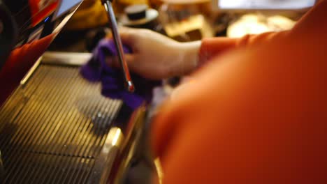 Close-up-on-hands-of-coffee-barista-using-coffee-machine-to-add-hot-milk-into-silver-jug