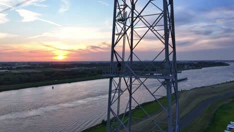 man preparing for a base jump from a transmission tower at sunset over a wide river