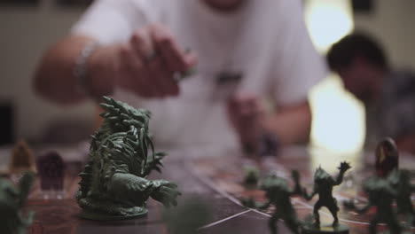 hand picking up green character from desk game, people in blurry background, closeup view