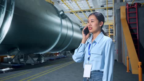 vista lateral de una mujer de negocios asiática hablando por teléfono móvil en una fábrica de fabricación de tubos