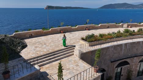 close drone circling woman walking along overlook of mamula island fortress walls and inner courtyard from above