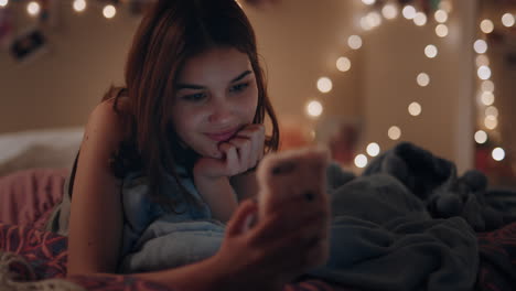 beautiful teenage girl lying on bed texting using smartphone browsing social media online chat enjoying evening relaxing at home