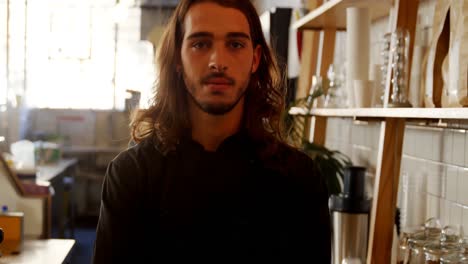 Confident-waiter-with-arms-crossed-standing-at-the-counter-4k