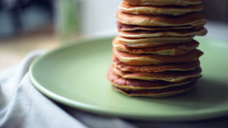 pancakes stack on green plate at kitchen table. close up of american pancakes