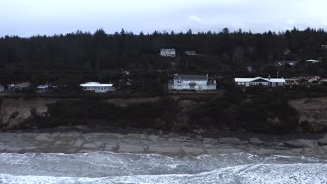 cliffside view of houses, seal rock in oregon coast, dark afternoon, wave from ocean shore, aerial pan view