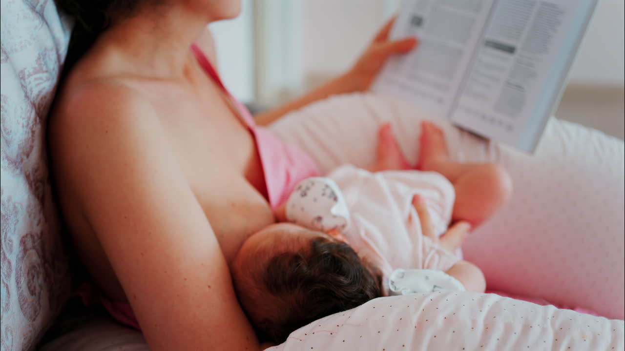 Intimate close up of a mother breastfeeding her baby while holding a book