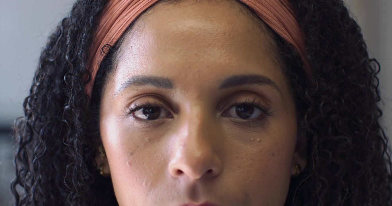 Donna afroamericana che apre gli occhi dopo aver sbattuto le palpebre in studio, indossa una fascia color ruggine, guance umide