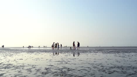 Low-angle-shot-capturing-the-beautiful-landscape-with-distance-tourists-barefoot-on-the-tidal-flats-enjoying-the-nature-at-famous-pristine-Gaomei-wetlands-preservation-area,-Taichung-city,-Taiwan