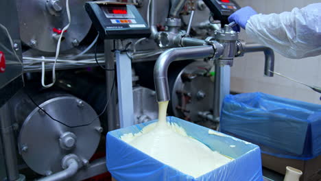 creamy white dairy substance being poured into the box covered with plastic bag. hand of the worker pushes the valve to stop pouring. filling another box with dairy product.