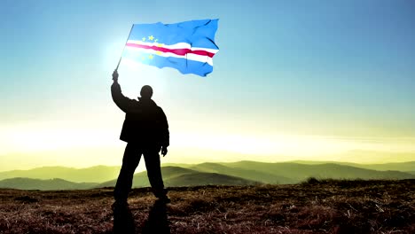 exitoso hombre silueta ganador agitando bandera de cabo verde en la parte superior del pico de la montaña. fondo de bucle cinemagraph