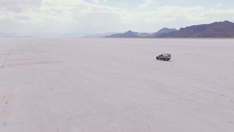 Truck driving on a vast salt flat desert with mountains in the background