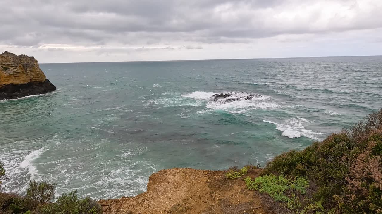 Visitors admire coastal views and informative signs along the Great Ocean Road under overcast skies