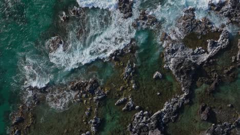 Ocean-waves-wash-over-rocks-by-North-Shore-of-Maui,-top-down-aerial-slo-mo