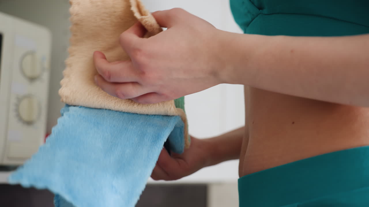 Pregnant Woman In Kitchen Nesting Chores, Holding Stack Of Towels Near Cabinets, Visible Microwave In Background, Gentle Hand On Belly, Calm Domestic Moment, Focused Preparation And Daily Maternity