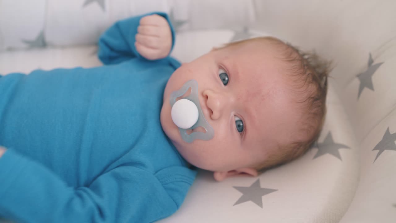 маленький мальчик с голубыми глазами пинает ноги, сосая манекен в коконе.