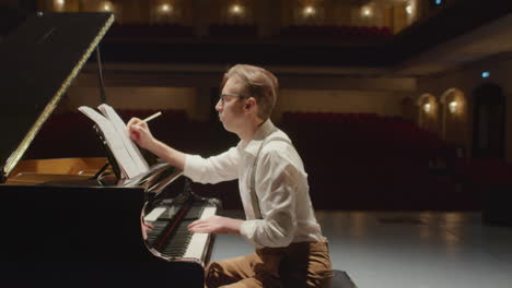 composer writing music at grand piano in concert hall