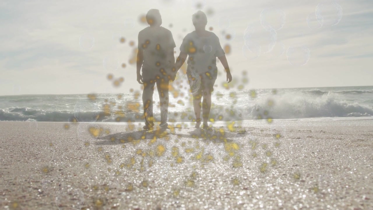 Senior couple walking toward camera on shore sun sparking warm specks hiding detail for travel ad