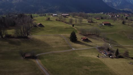 Lush-green-grass,-farmland-buildings,-aerial-reveal-snow-covered-mountain