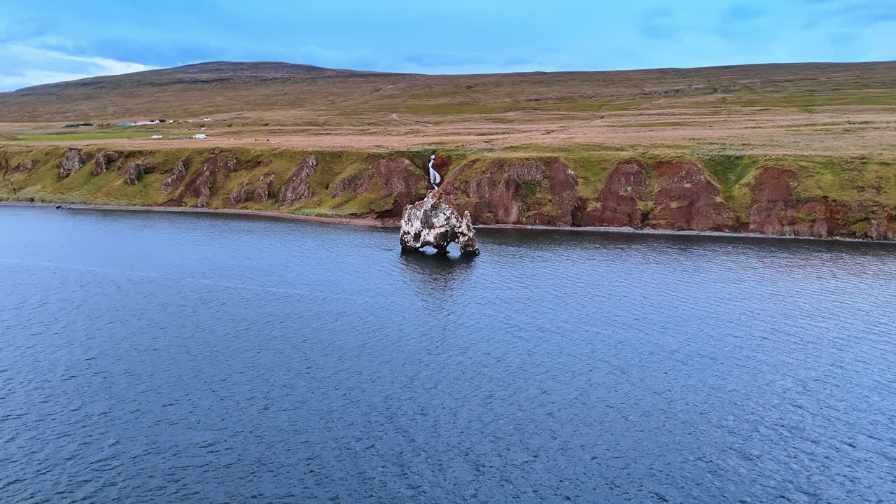 Crooked rock standing on three feet in the waterscape near the coast of Iceland. Distancing from rocky shore and flying over the North Atlantic Ocean.