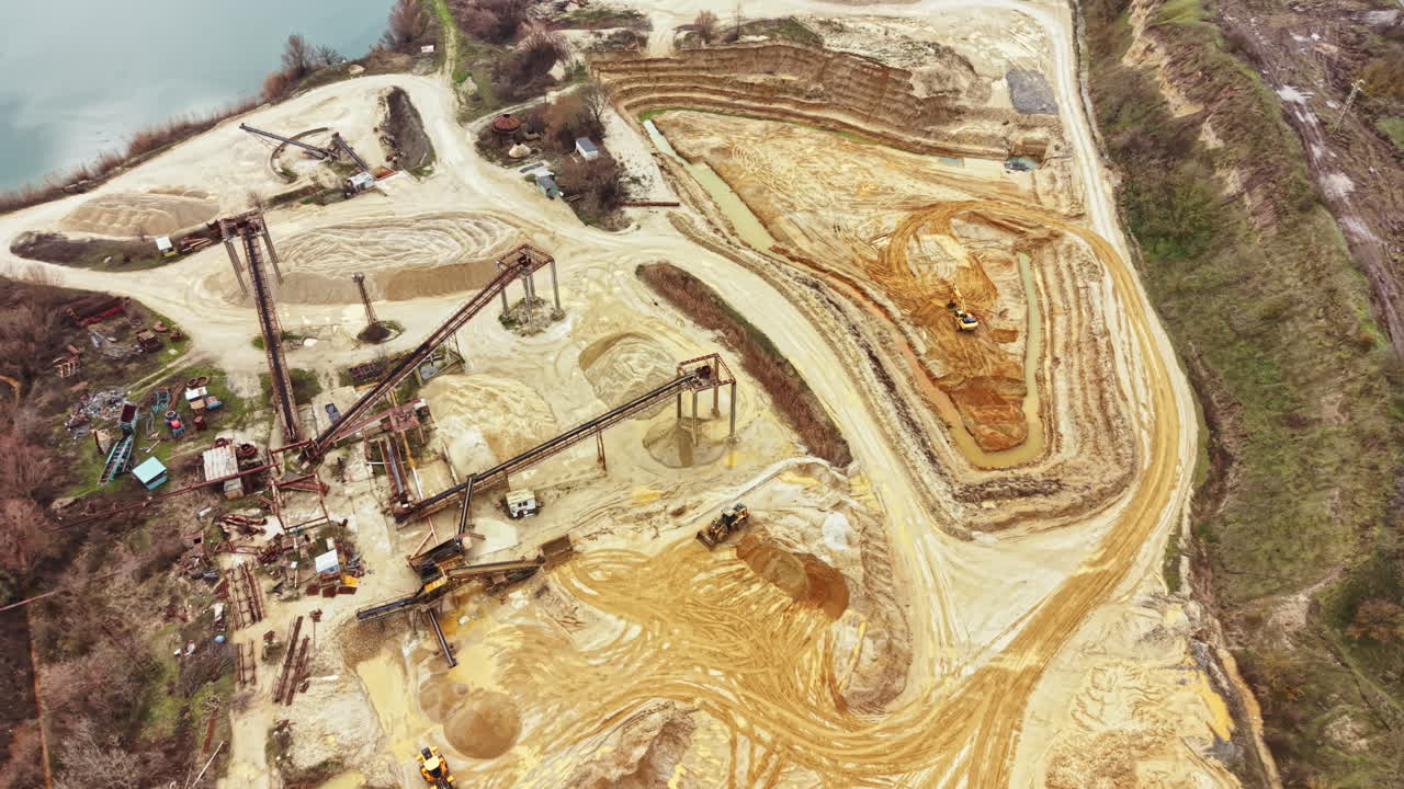 Construction site in active operation with machinery moving soil and materials near a river during daylight hours