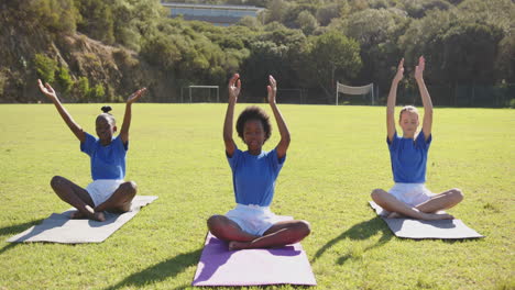 practicing yoga, three girls sitting on mats in school field outdoors