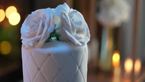 wedding cake made of white fondant, with edible pearls and large roses on top, romantic decorated atmosphere with candles