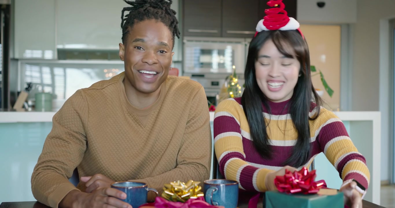 African American man and Asian woman speaking to camera at kitchen table, exchanging mugs and gift