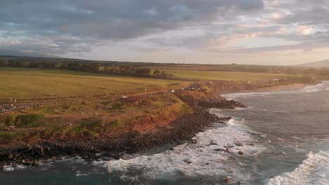 a drone flies over the ocean waves and into maui hawaii's ho'okipa beach overlook at sunset near paia