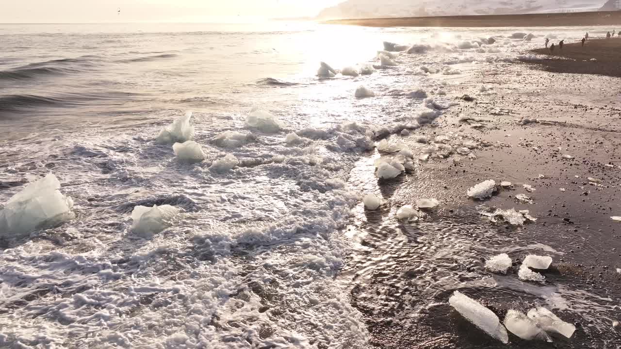 Glacial ice glistens on black sand shore as waves crash on Diamond Beach Iceland
