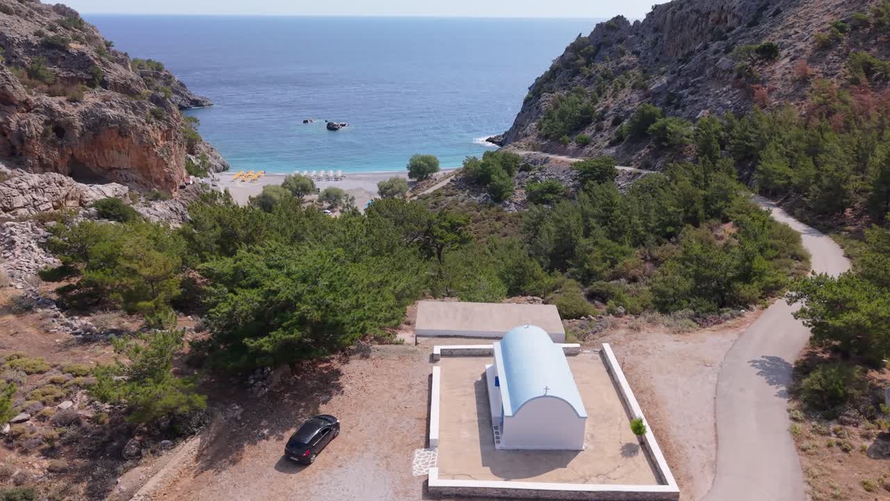 Aerial drone ascending behind a chapel to reveal Achata Beach and the surrounding seascape in Karpathos, Greece