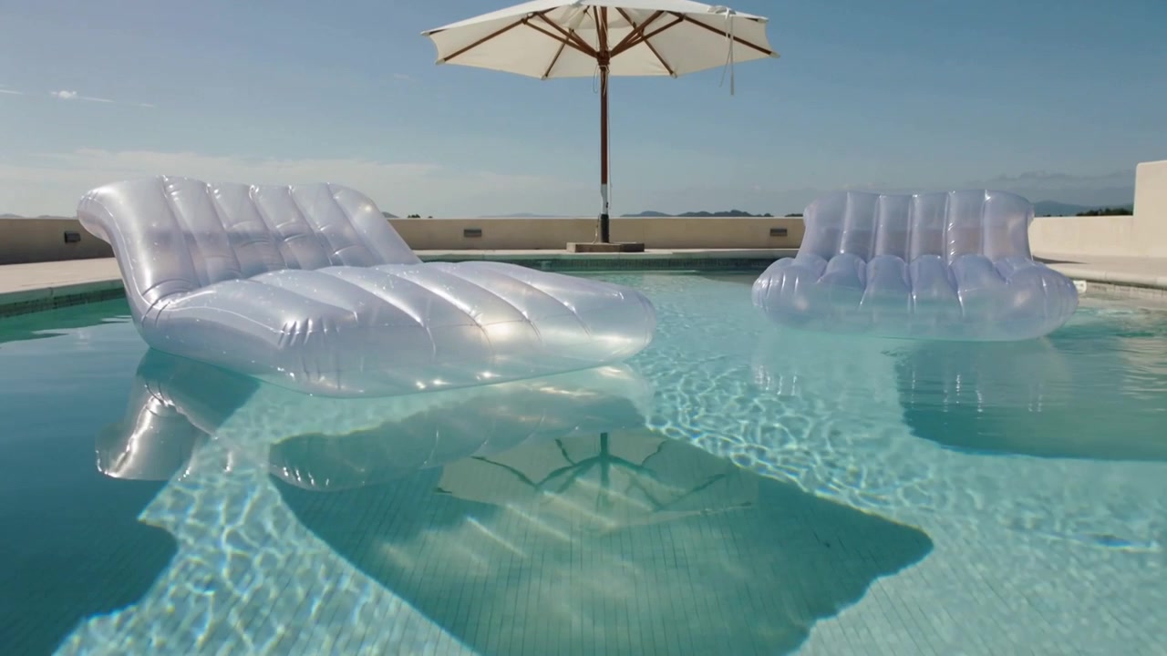 Moving camera bringing two clear floats drifting in rooftop pool, showing white umbrella reflection