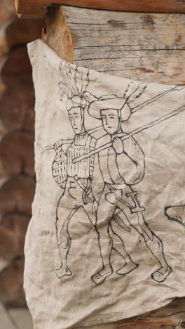 drawing of couple of travelers and big boot on rectangular piece of cloth fixed on wall of wooden house. medieval sign indicating shoemaker workshop