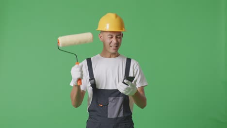 asian man painter wearing safety helmet looking at smartphone then screaming goal celebrating while standing in the green screen background studio