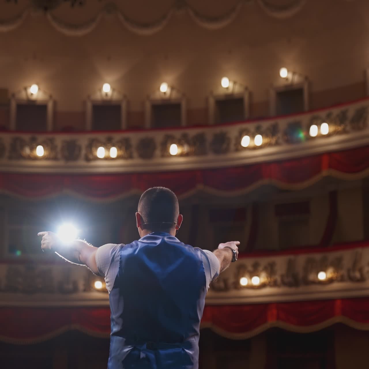 Actor on theater scene with his back to the camera. Man on stage bowing and actively gestures with his hands. Back view.
