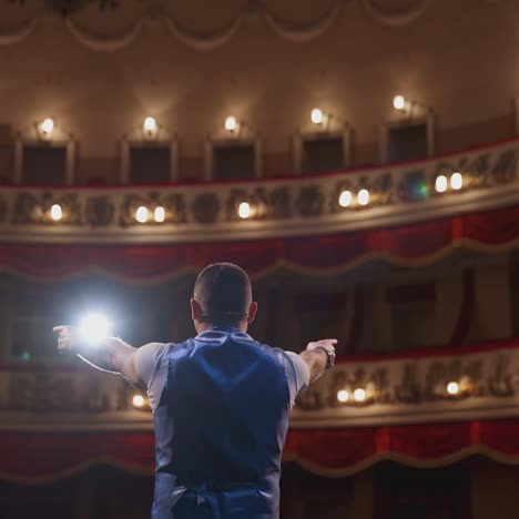 actor on theater scene with his back to the camera. man on stage bowing and actively gestures with his hands. back view.