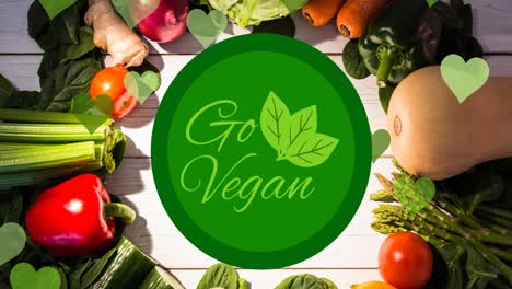 animación de texto go vegan en verde con logotipo de hojas, sobre verduras frescas en tablas blancas