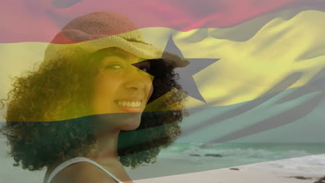 animación de la bandera de ghana ondeando sobre una mujer afroamericana sonriente disfrutando de la brisa en la playa