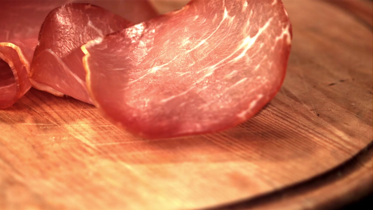 Fette sottili di salumi che cadono su un tagliere di legno