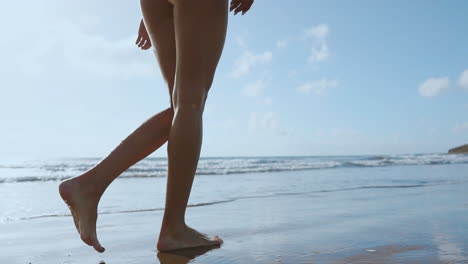 Woman-bare-foot-walking-on-the-summer-beach.-close-up-leg-of-young-woman-walking-along-wave-of-sea-water-and-sand-on-the-beach.-Travel-Concept.