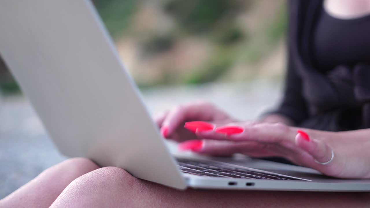 mujer de negocios exitosa con manicura roja brillante escribiendo en el teclado de la computadora portátil al aire libre en la playa con vista al mar. cerca de las manos de la mujer escribiendo en la computadora. freelance, nómada digital, viajes y vacaciones