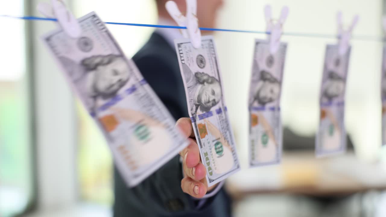 Biznesmen dotyka mokrych banknotów dolarowych wiszących na sznurku do bielizny.